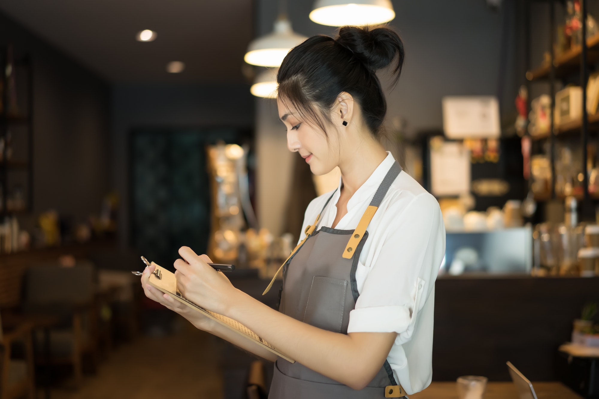 Attractive beautiful caucasian barista with list checking stock at front counter in coffee shop.