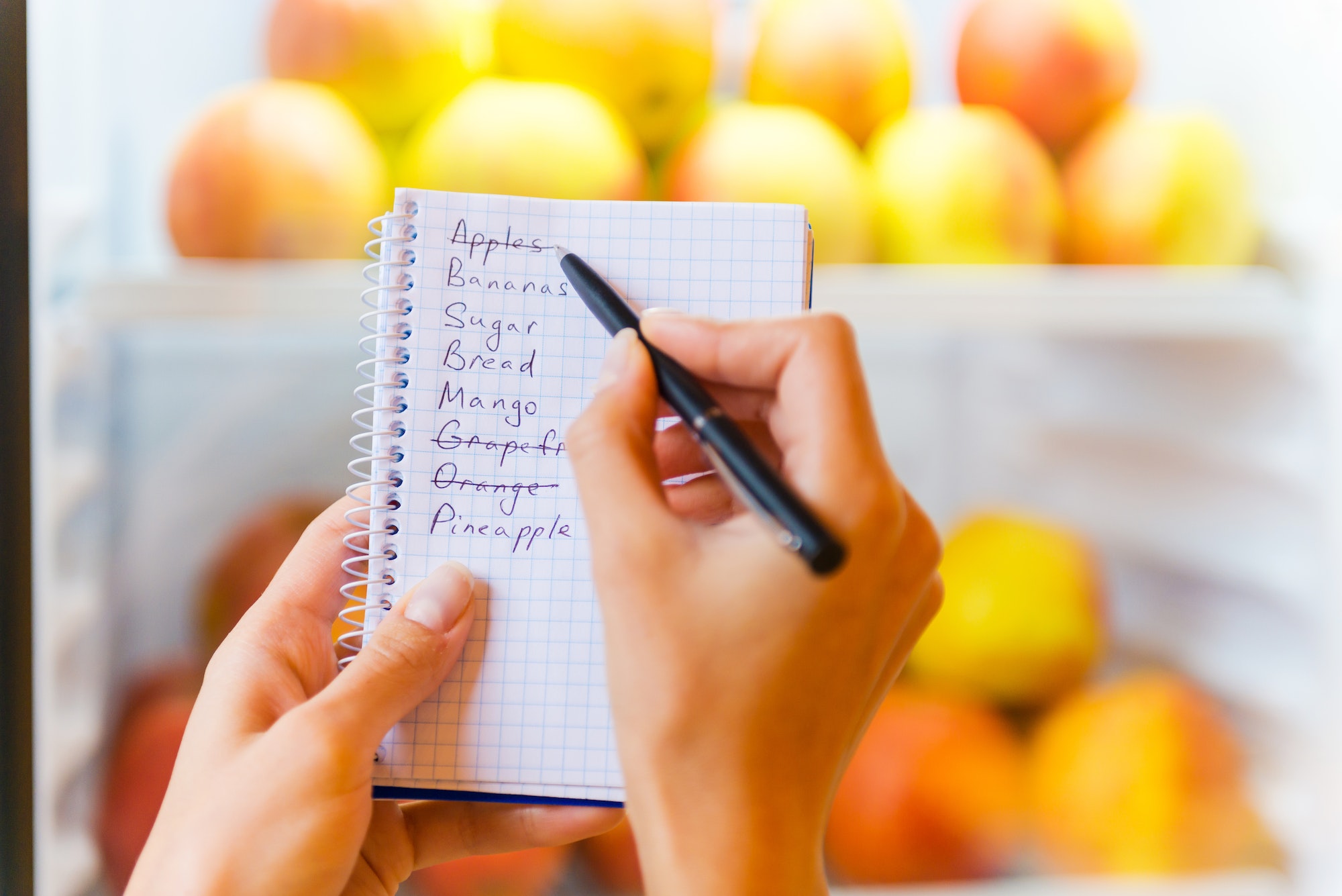 Checking shopping list. Close-up of woman checking shopping list with apples in the background